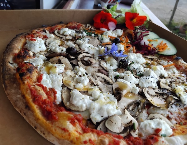 la pizza au chèvre et miel agrémenté de fleurs comestibles et crudités de saison , dans une boîte à pizza